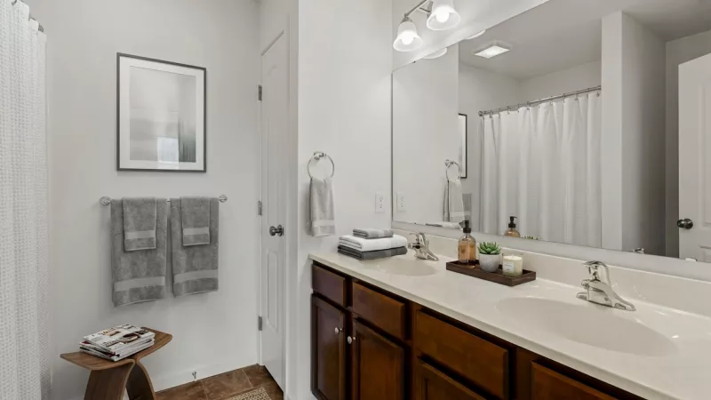 Modern bathroom with a dark wood double vanity, white sinks, large mirror, framed art, and a shower area. Towels and decor.