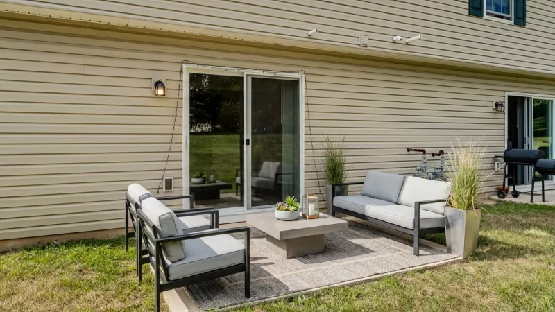 Outdoor patio with gray seating, coffee table on a wooden deck next to a beige house and sliding door.