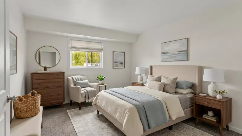 Bright, neutral bedroom with a beige bed, two nightstands, a wooden dresser with a mirror, and an armchair.
