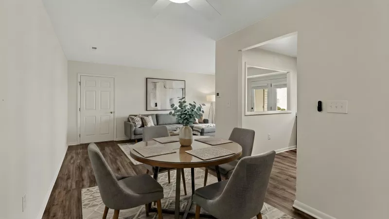 Open concept dining area with a round wood table, four gray chairs, and a living room visible in the background.