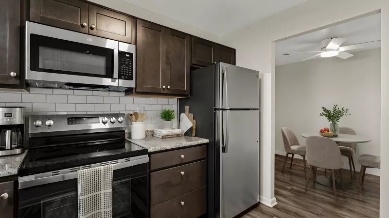 Modern kitchen with dark wood cabinets, stainless steel appliances, white subway tile, and a dining area beyond.