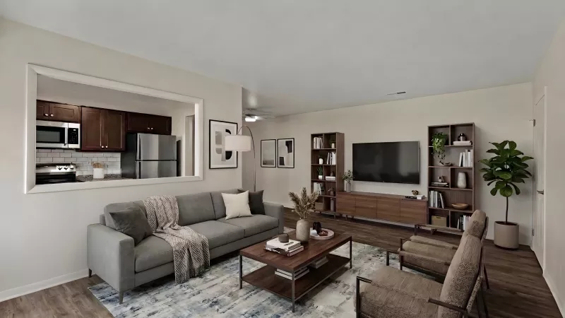 Modern living room with a gray sofa, coffee table, TV, bookshelves, and two armchairs. Kitchen seen through a wall cutout.