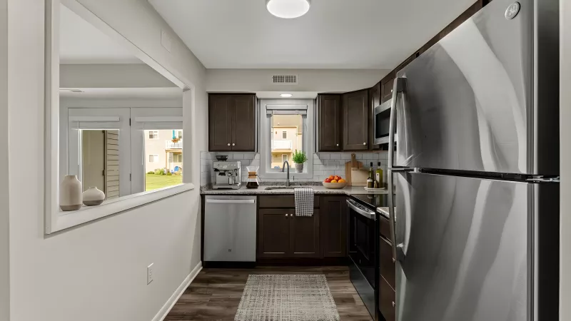 Modern kitchen with dark brown cabinets, stainless steel appliances, dark wood floor, and a pass-through window.