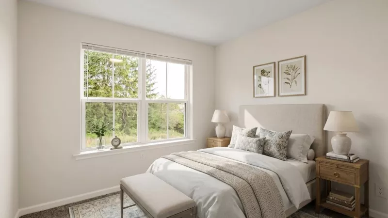 Bright bedroom with a bed, two lamps on rustic nightstands, and a large window overlooking green trees.