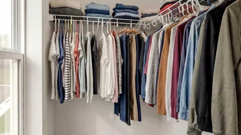 Organized walk-in closet with a window, shelves of folded clothes, and hanging garments.