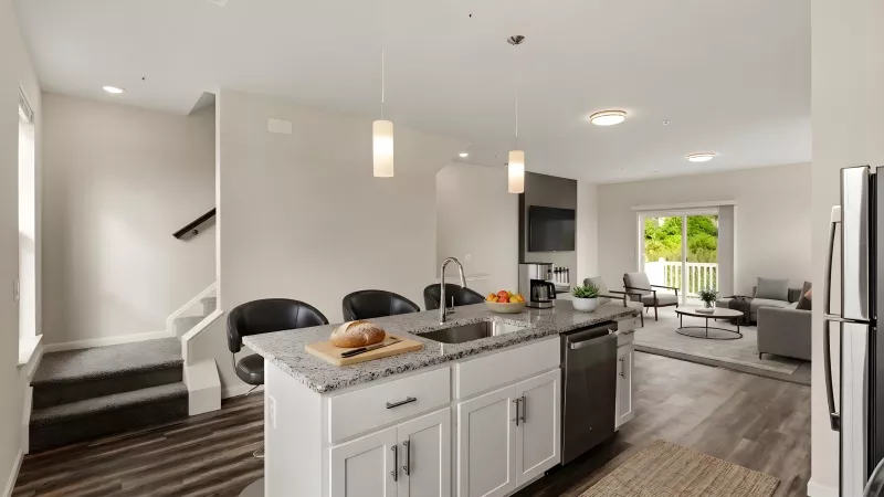 Spacious apartment interior featuring a kitchen island with stools, a living area with a couch, and a staircase leading upstairs.