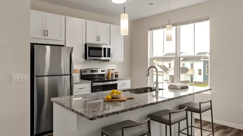 Modern kitchen with white cabinets, stainless steel appliances, and a granite island with three stools and a sink.