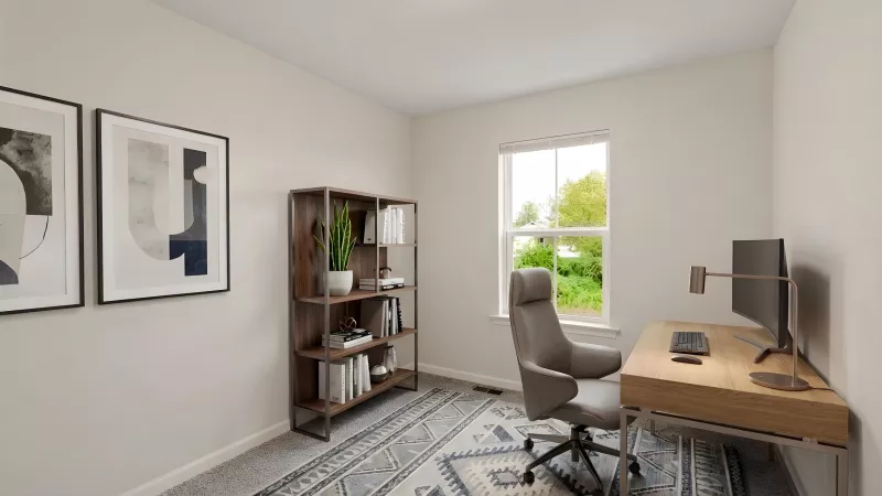 Bright modern home office with a light wood desk, grey ergonomic chair, dark bookshelf, abstract art, and patterned rug.