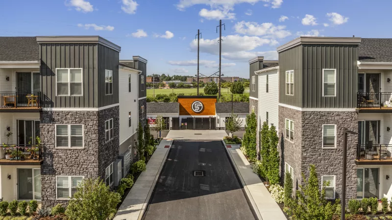 Aerial view of modern apartment buildings with stone and grey facades, lining a street leading to garages and storage.