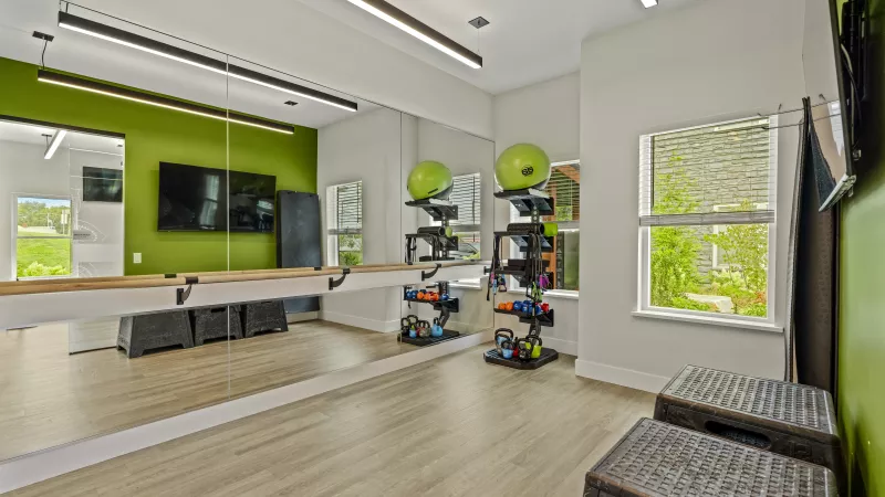 Bright gym with a green accent wall, large mirrors, colorful weights on shelves, and two exercise steps.