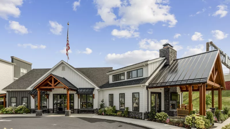 Modern white and dark gray building with wooden accents, a prominent entryway, a dark roof, and an American flag.