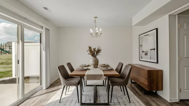 Dining room with a wooden table, six gray chairs, a light patterned rug, and a sliding glass door to a green yard.