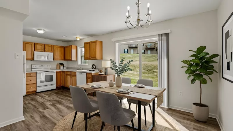 Open-concept kitchen with light wood cabinets, white appliances, dining table with chairs, and a sliding door.