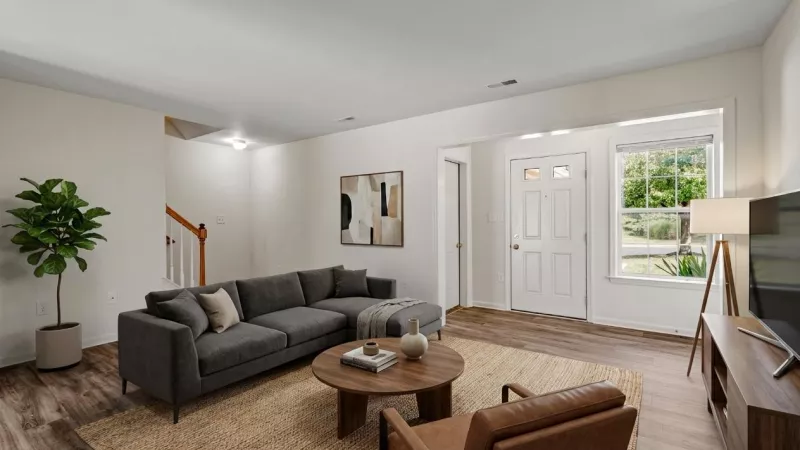 Modern living room with gray sectional sofa, round coffee table, brown armchair, and white front door.