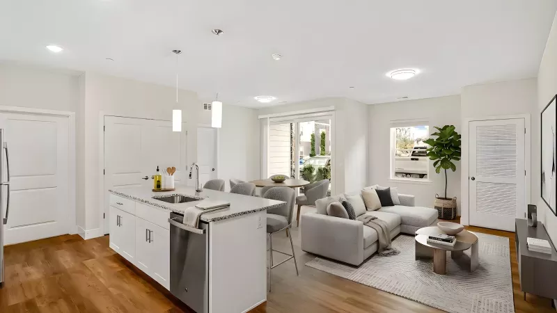 Modern open-plan kitchen, dining, and living room with white cabinets, gray sectional sofa, and hardwood floors.