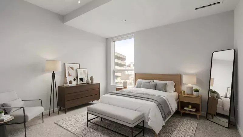 Bright bedroom with a wooden bed, bench, dresser, armchair, and a full-length mirror.