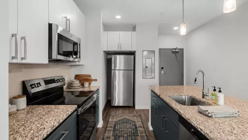 Bright, modern kitchen featuring white and grey cabinets, stainless steel appliances, granite countertops, and an island sink.