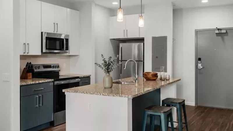 Sleek kitchen with white and grey cabinets, stainless steel appliances, granite island, two stools, and pendant lights.