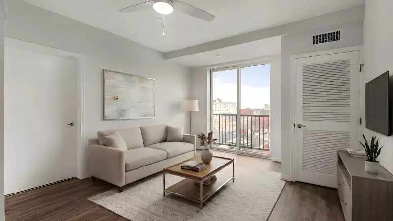 Modern living room with a beige sofa, wood coffee table, and large window leading to a balcony with a city view.