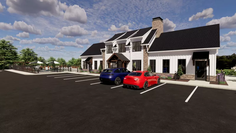 Modern white building with black roof and stone chimney. Two cars are parked in the asphalt lot under a blue sky. 