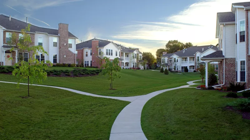 Apartment complex with beige buildings and brick accents, green lawn, and a split path at sunset.