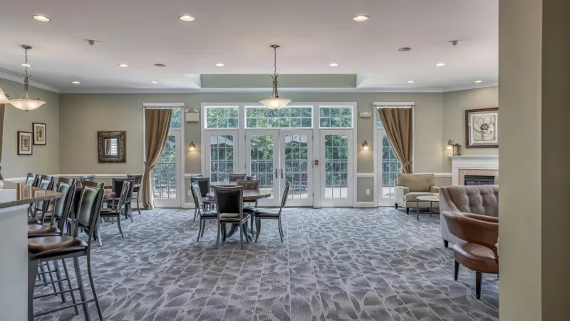 Bright community lounge with patterned carpet, diverse seating, light green walls, a fireplace, and large glass doors.