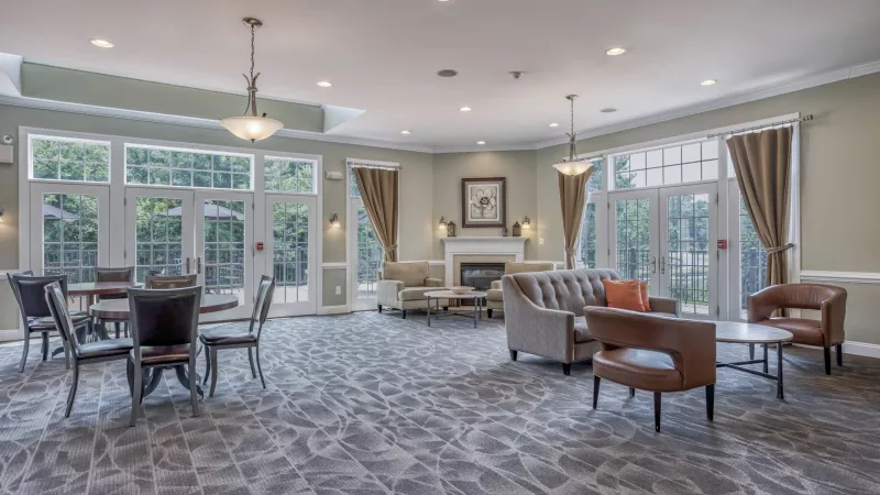 Spacious common room with various seating arrangements, a fireplace, and large windows looking outside.