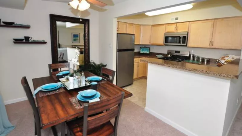 Apartment dining room with a dark wood table and four chairs, open to a kitchen with light cabinets and steel appliances.