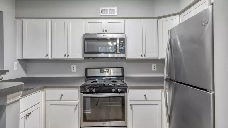 Modern kitchen with white cabinetry, gray countertops, and stainless steel refrigerator, gas range, and microwave.