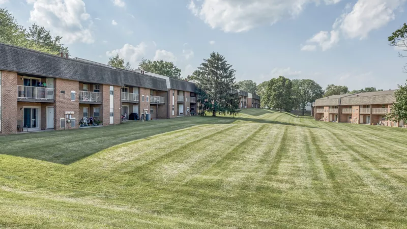 Photograph of a multi-building apartment complex with brick facades, balconies, and a wide, mown green lawn.