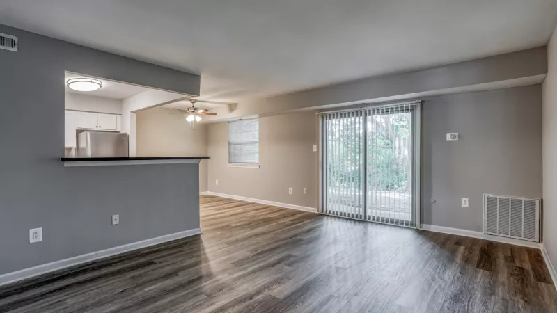 Living room with dark wood floor, light gray walls, sliding glass door, and pass-through to kitchen.