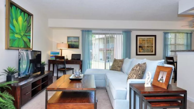 Bright living room with light blue sectional, dark wood furniture, green abstract art, and sliding glass doors to patio.