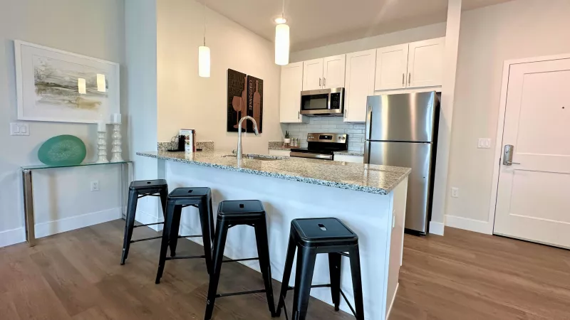 Contemporary kitchen with granite countertops, pendant lighting, and bar seating for three, opening to the front entry and living room.