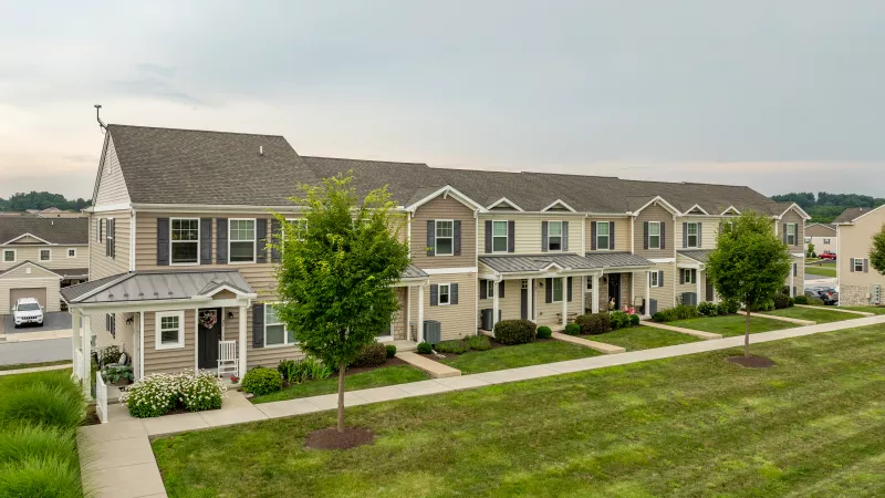 Exterior view of the Penn Grant Commons community clubhouse, featuring stone columns, covered entry, and manicured landscaping.