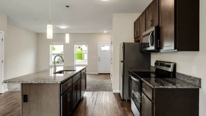Open kitchen at The Reserve at Willow Ridge apartments with granite countertops, stainless steel appliances, and center island with pendant lighting.