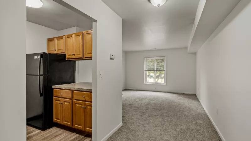 Open layout at Rosedale Apartments showing kitchen with wood cabinetry and living space with carpet flooring
