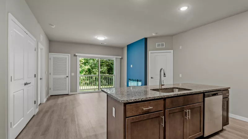 Open floor plan at Signature Flats at Hershey apartments showing granite island kitchen, stainless steel appliances, and living room with balcony access