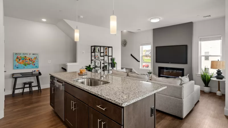 Open-concept kitchen and living room at The Reserve at Timber Ridge Apartments with granite island, pendant lighting, and fireplace.