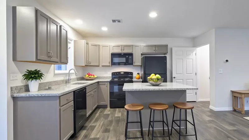 Modern apartment kitchen with gray cabinetry, granite countertops, black appliances, a central island with bar seating, and durable wood-look vinyl plank flooring.