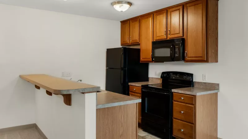 Galley kitchen with wood-toned cabinetry, black appliances including refrigerator and range, breakfast bar, and tile flooring.