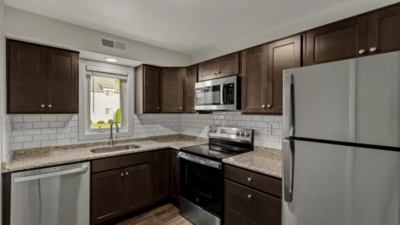 Kitchen at Pioneer Woods Apartments with stainless steel appliances, granite counters, and a window providing natural light.