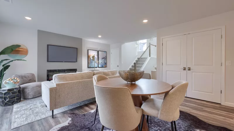 Spacious living area at The Pond Apartments with round dining table, modern chairs, neutral sectional sofa, and accent artwork near the staircase.