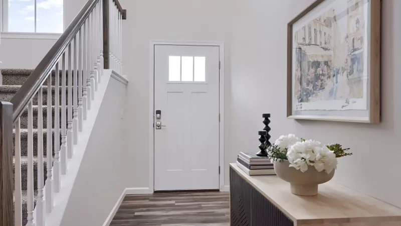 Entryway at The Pond Apartments showcasing a white front door, staircase with wood railing, decorative console table, and framed artwork.