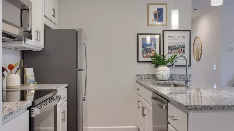Kitchen at The Pond Apartments with granite countertops, stainless steel appliances, white subway tile backsplash, and framed wall art.