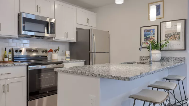 Modern kitchen at The Pond Apartments featuring stainless steel oven, microwave, and refrigerator with pendant lighting above a granite breakfast bar.