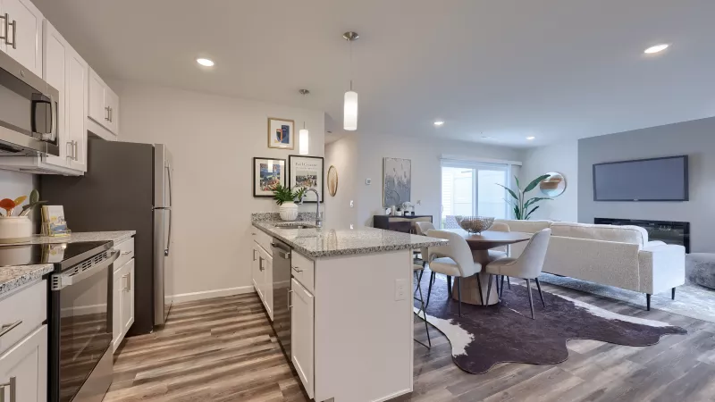 Open-concept kitchen and dining area at The Pond Apartments with granite countertops, pendant lighting, and a round wooden dining table.