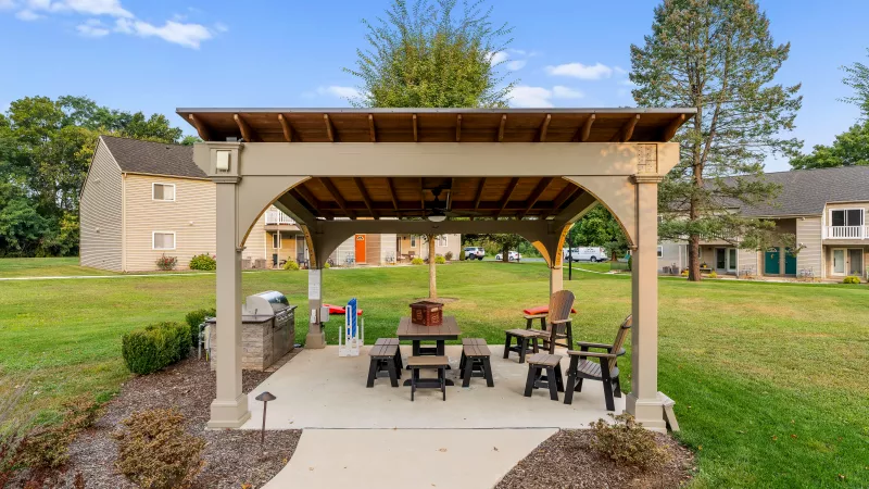 Covered outdoor gazebo with seating and a built-in grill, set on landscaped grounds with walking paths and green lawns.