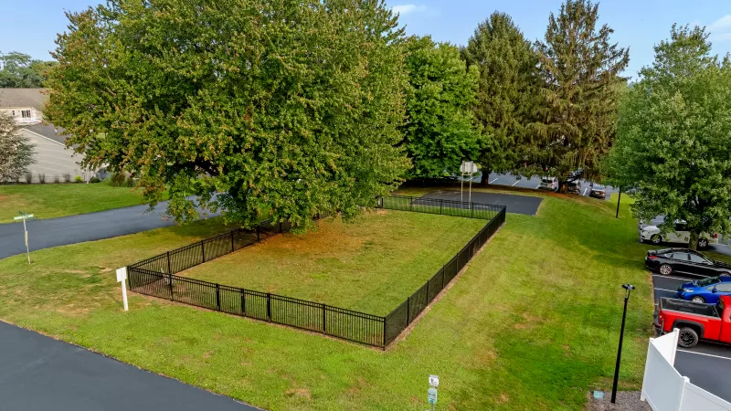 Fenced dog park shaded by large trees, located near community parking and walking paths.