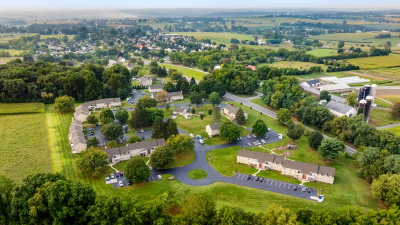 Aerial view of apartment community with multiple buildings, landscaped green spaces, and parking lots, set within a rural neighborhood.