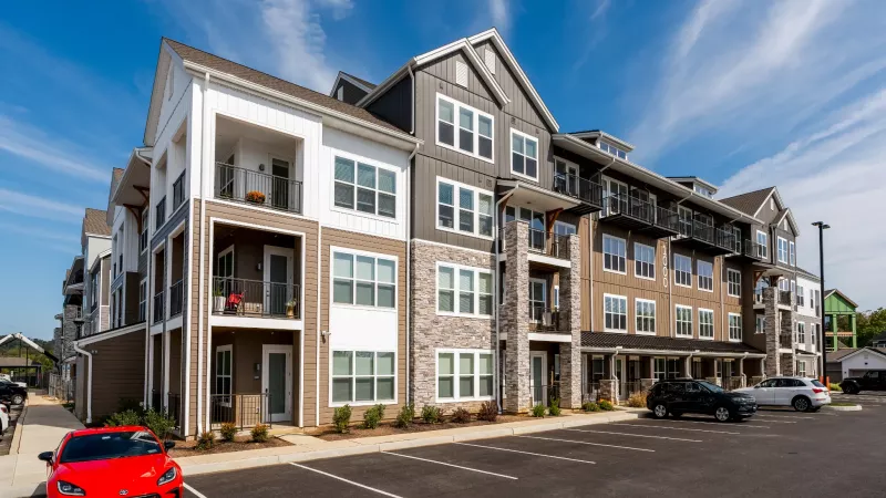 Straight-on view of a four-story apartment community with modern architecture, metal awnings, and convenient front parking.